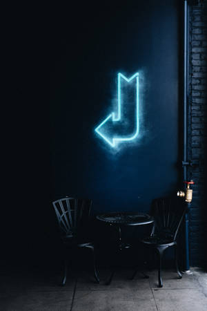 Et glødende blåt neonskilt i en mørk gyde med metalstole og bord. — Blå Wallpapers