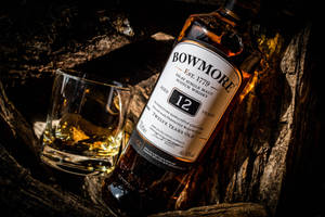 En flaske Bowmore whisky og glass i en tretønne med varm belysning. — Whiskey Bakgrunner
