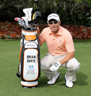 O golfista Brian Davis posa com a sua bolsa de golfe num campo de golfe ensolarado. — Erva Papéis de Parede