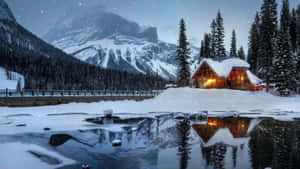 Acogedora cabaña brillando en la nieve con reflejo de la montaña en lago helado por la noche — Inicio Fondos de pantalla