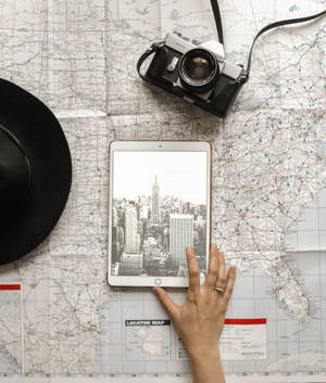 Hand houdt tablet met stadsilhouet over reiskaart met camera en hoed. — Camera Achtergronden