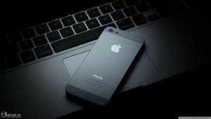 Silver iPhone on a laptop keyboard in dim lighting — iPhone 8 Wallpaper