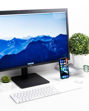 Modern minimalist desk with computer monitor showing mountain wallpaper and phone beside it. — iPhone Xs Wallpaper