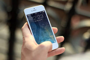 Hånd som holder hvit iPhone med stjerneklar nattbakgrunn og opplåsingsprompt. — Mobile Bakgrunner