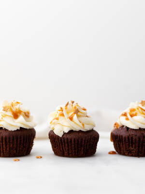 Tres cupcakes de chocolate con caramelo y glaseado blanco sobre mármol. — Cupcake Fondos de pantalla