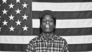 Young man wearing a checkered cap and plaid shirt standing in front of an American flag. — Cool Rap Wallpaper