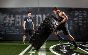 Athlete rolling heavy tire in gym with chalkboard wall behind. — Gym Wallpaper