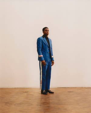 Mann in einem blauen Gucci-Anzug, der in einem minimalistischen Studio mit Holzboden steht. — Caesar Wallpaper