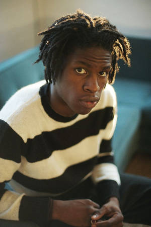 Junger Mann mit Dreadlocks in gestreiftem Pullover schaut in die Kamera drinnen — Caesar Wallpaper
