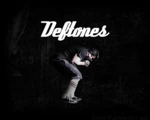 A crouching musician with Deftones text in a dark gritty background. — Deftones Wallpaper