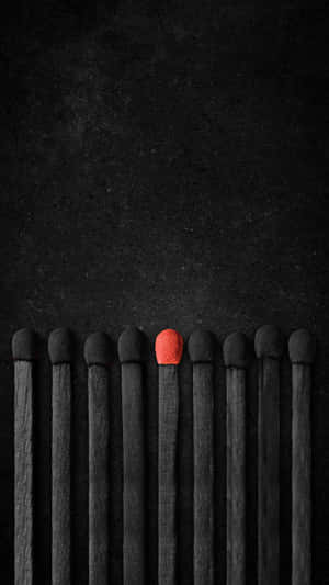 One red match head among blackened matches on dark textured surface. — Disparate Wallpaper