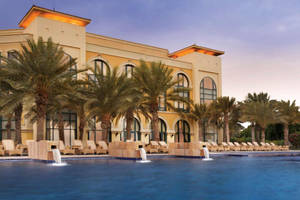 Luxury resort pool with palm trees and lounge chairs at dusk. — Hotel Wallpaper