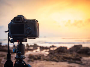 Camera op statief gericht op de oceaan bij gouden zonsondergang — Camera Achtergronden