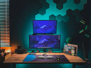 Gaming-Schreibtisch mit zwei Monitoren und tealfarbener Beleuchtung vor sechseckigen Wandpaneelen. — Desktop computer Wallpaper