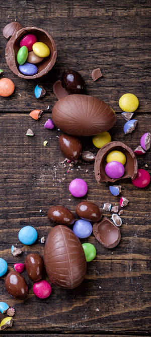 Broken chocolate eggs revealing colorful candies on a wooden table. — OnePlus 11 Wallpaper