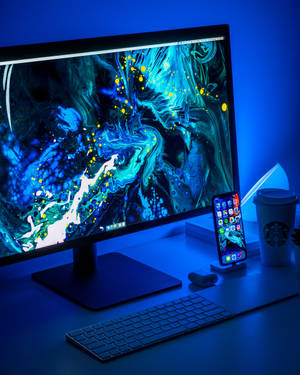 Modern tech workspace with glowing monitor and phone under blue ambient light. — iPhone Xs Wallpaper