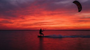 Kitesurfista surfeando olas al atardecer con cielo rojo vibrante