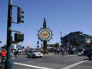 Folkemængder krydser en travl gade nær Fisherman's Wharf-skiltet i San Francisco på en solskinsdag. — Gade Wallpapers