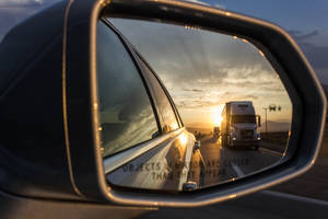 Bils sidespejl, der reflekterer en lastbil på en ørkenmotorvej ved solnedgang. — Lastbil Wallpapers