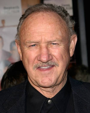 Skuespilleren Gene Hackman smiler til en formell begivenhet iført en mørk dress. — Hollywood Bakgrunner
