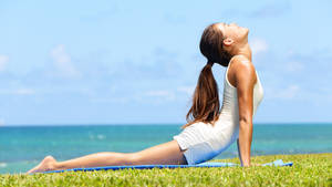 Woman practicing yoga on grass near ocean under clear sky — Yoga Wallpaper