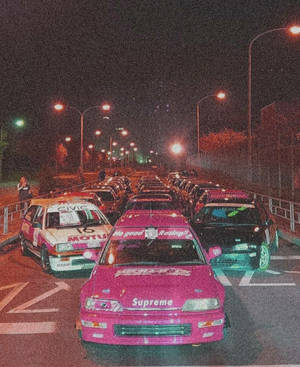 Pink racerbil med Supreme-logo parkeret om natten med andre modificerede biler. — Gade Wallpapers