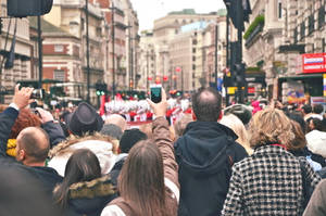 Crowd watching parade in city street holding up phones to record. — Travel Wallpaper