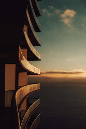 Moderne bygning med buede altaner med udsigt over havet ved solnedgang. — Apple Wallpapers