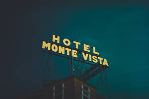 A glowing yellow hotel sign against a dark teal sky at night. — Hotel Wallpaper