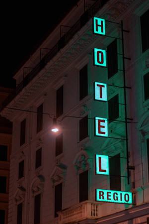 Neon hotel sign glowing green on a building at night. — Hotel Wallpaper