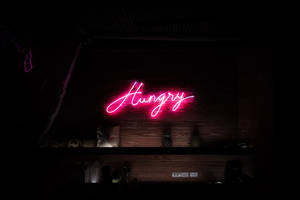 Pink neon sign reading 'Hungry' on a dark wood wall above a bar shelf. — Tiny Tan Bts Wallpaper