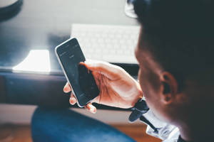 Person bruker smarttelefon ved skrivebord med tastatur i bakgrunnen. — Mobile Bakgrunner