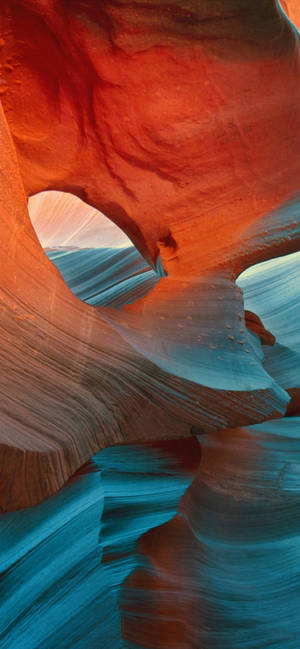 Slot canyon with red and blue rock formations illuminated by sunlight. — iPhone 13 Pro Max Wallpaper