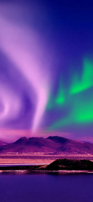 Purple and green aurora lights glow over mountains and water at night. — iPhone 13 Pro Max Wallpaper
