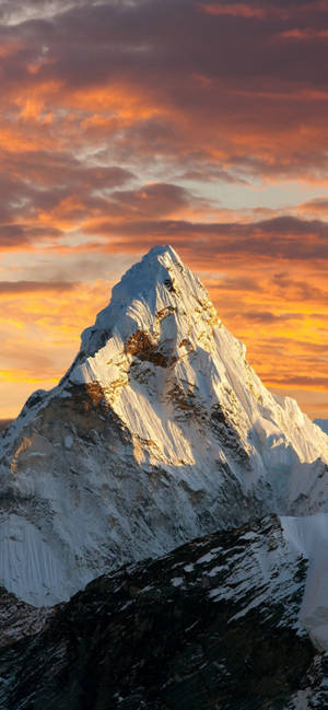 Snowy mountain peak bathed in golden sunset light against vibrant orange and purple clouds. — iPhone 13 Pro Max Wallpaper