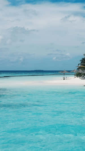 Tropical beach with turquoise water and white sand under a cloudy sky. — iPhone 8 Plus Wallpaper