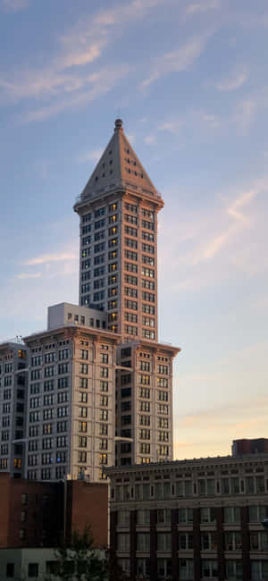 Smith Tower Seattle skyscraper at sunset with warm lighting and blue sky — iPhone 13 Mini Wallpaper