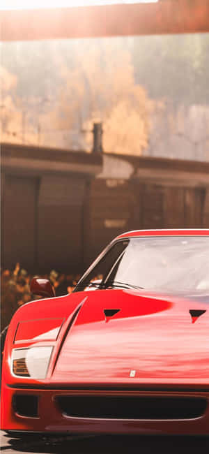 Red Ferrari sports car in golden sunlight with blurred rustic building behind. — iPhone 13 Mini Wallpaper