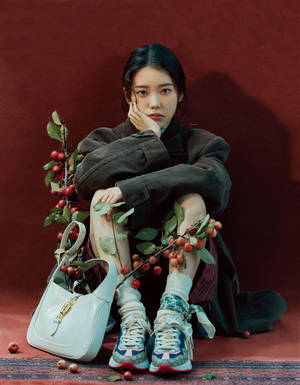 Junge Frau in modischem Outfit sitzend mit Beeren und Handtasche vor rotem Hintergrund. — Iu Wallpaper