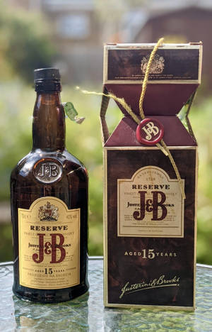 En flaske og boks med J&B Reserve 15 år gammel whisky på et glassbord utendørs. — Whiskey Bakgrunner