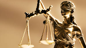 Blindfolded Lady Justice statue holding balanced scales in golden hue. — Justice Wallpaper