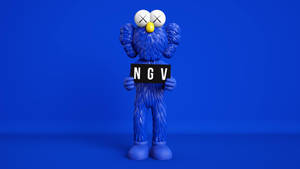 Patung KAWS berbulu biru memegang papan NGV di lingkungan studio. — Kaws Wallpaper