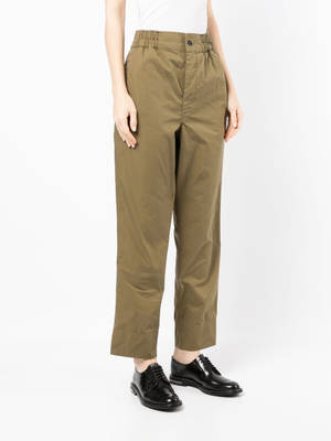 Pessoa em calças verde-oliva e sapatos pretos em pé contra fundo branco — Moda Papéis de Parede