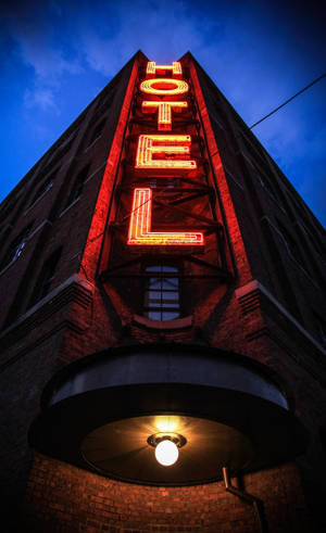 A brick hotel building with a glowing red neon sign at dusk. — Hotel Wallpaper