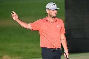 Golfspelare i orange skjorta och keps gestikulerar på grön bana — Wave Bakgrundsbilder