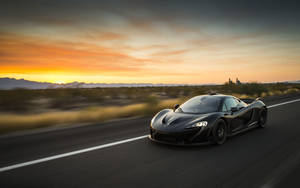 Supercar McLaren nera che sfreccia sull'autostrada del deserto al tramonto. — Auto Sfondi