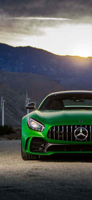 Carro esportivo Mercedes-AMG GT verde estacionado perto de turbinas eólicas com montanhas ao pôr do sol. — Clássico Papéis de Parede