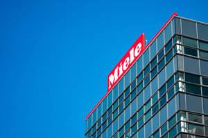 Edificio moderno de vidrio con letrero rojo de Miele contra cielo azul — Logo Fondos de pantalla