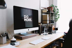Minimalistisk hjemmekontor med iMac, der viser 'DO MORE', og potteplanter nær vinduet. — Monitor Background