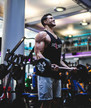 A fit man lifting weights in a gym with colorful equipment. — Barbell Wallpaper